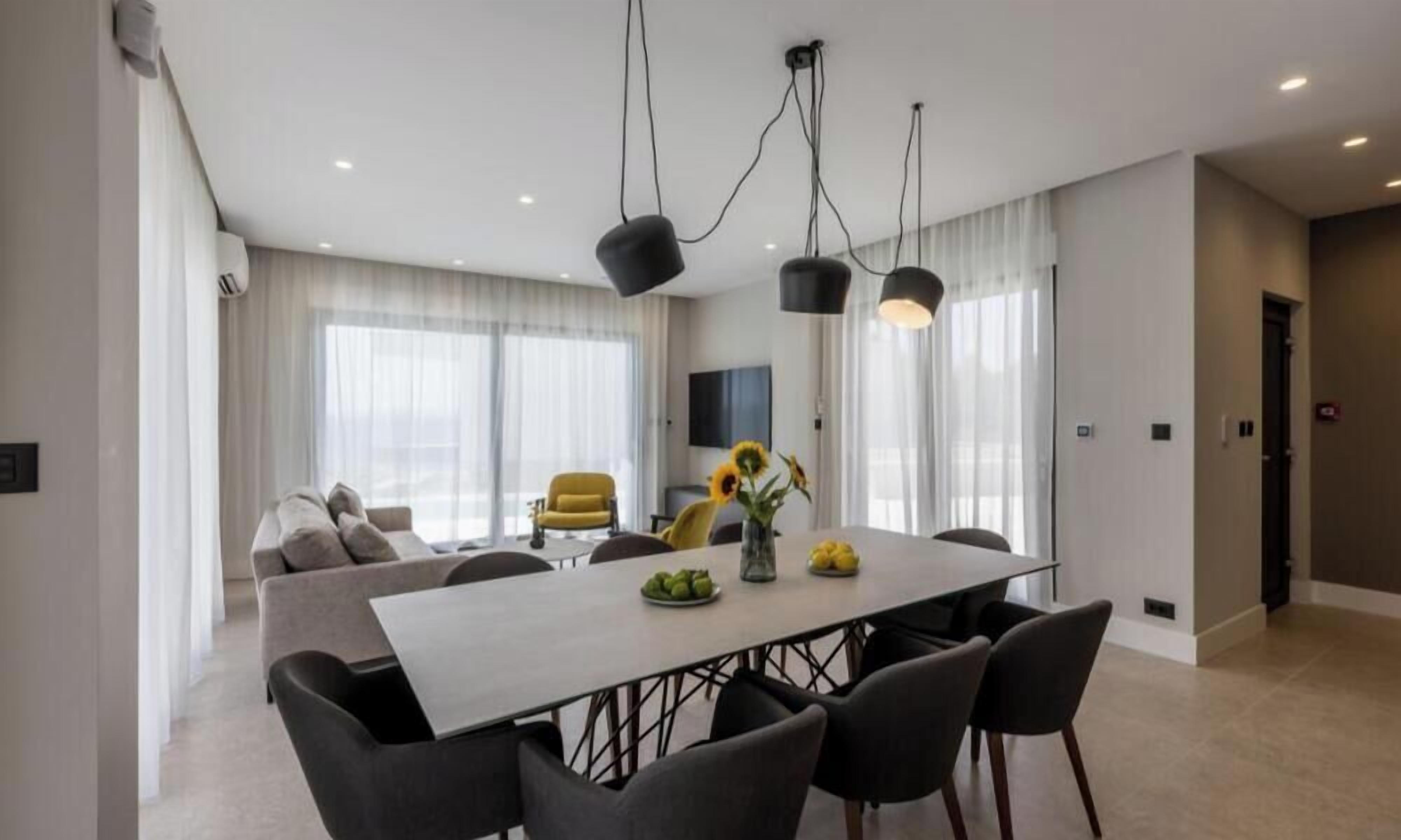 A modern dining area with a large table, chairs, and pendant lights.
