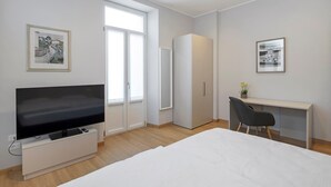 Et moderne hotelværelse med seng, fjernsyn, skrivebord, stol, garderobeskab og billedkunst på væggene.