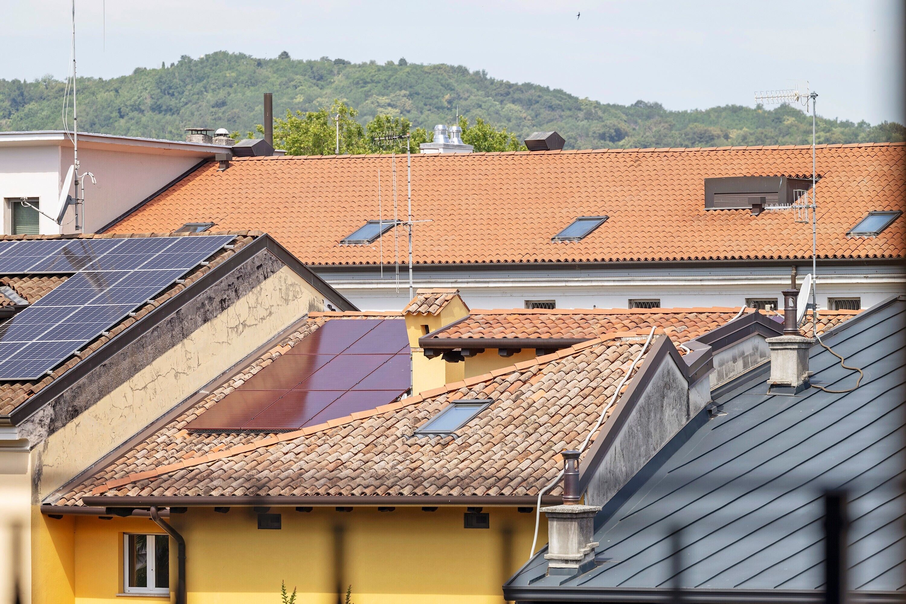 A building with multiple solar panels, a tiled roof, and a view of a green hill.