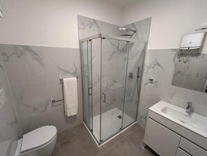 Un baño moderno con ducha envuelta en vidrio, inodoro, lavamanos y espejo.