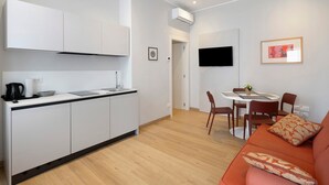 En kompakt opholdsstue med tekøkken, spiseplads og siddeområde.