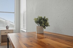 Ein Holztisch mit einer weißen Vase, in der eine Pflanze steht, platziert in der Nähe eines Fensters mit Jalousien.