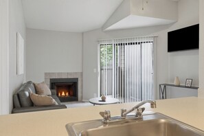 Una sala moderna con chimenea, un sofá, una mesa redonda y una zona de cocina con un lavamanos.