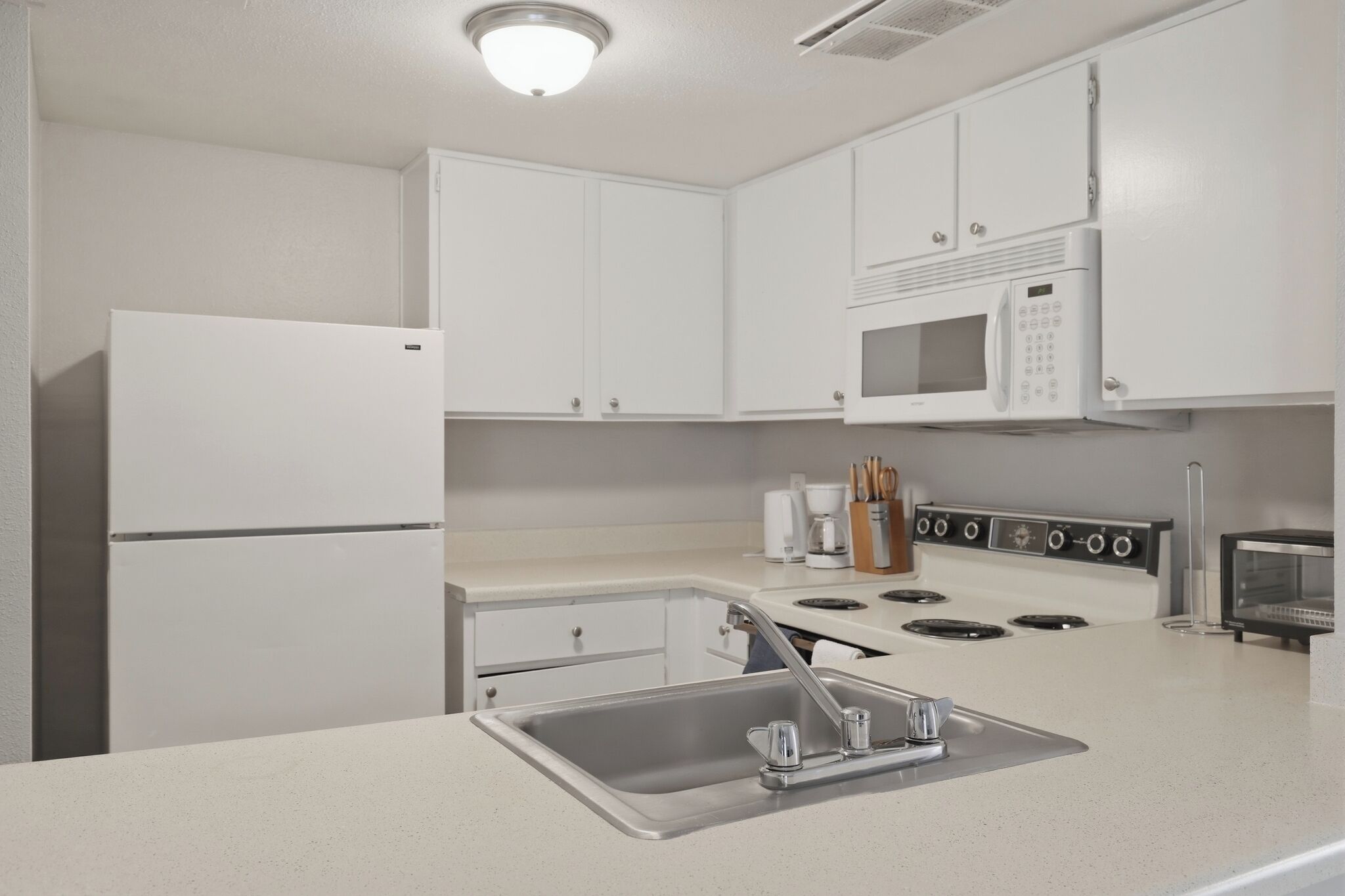 Een moderne keuken met witte kasten, een roestvrijstalen spoelbak, een inbouwmagnetron en een fornuis.