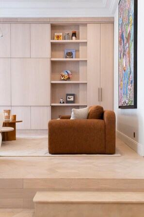 Ein modernes Wohnzimmer mit einem braunen Sofa, einem Bücherregal mit verschiedenen Gegenständen und einem großen abstrakten Gemälde an der Wand.