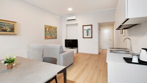 Un apartament modern amb zona de menjador, un sofà gris, televisió de pantalla plana, cuina amb rentapeus i fogó, i obra d'art a les parets.