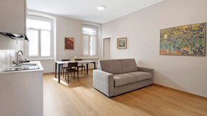 Un saló modern amb un sofà gris, una taula de menjador amb caires, una zona de cuina amb un rentapeus i un quadre gran a la paret.
