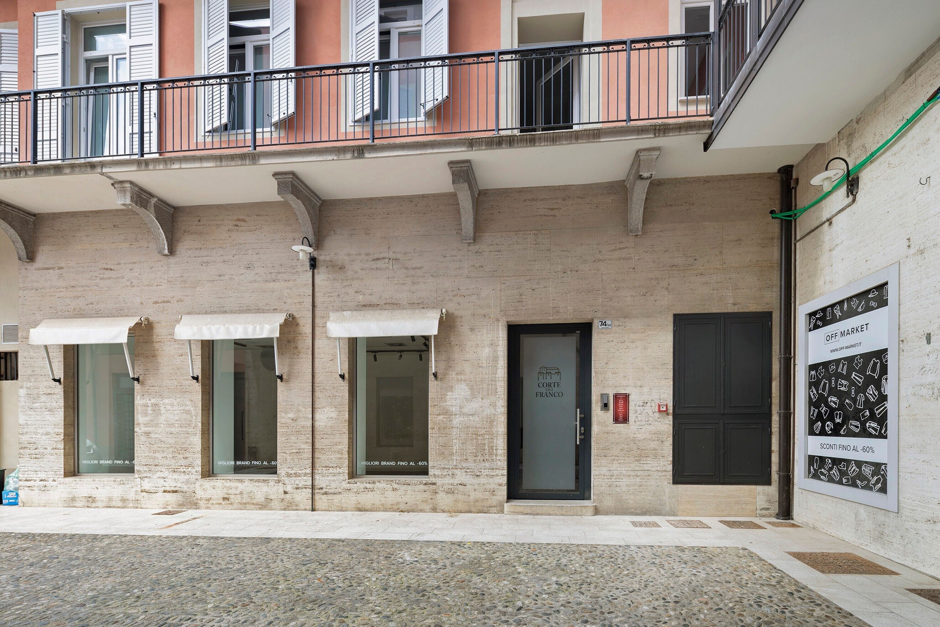 A building facade with a stone exterior, a black door with a sign, and a balcony with metal railings.