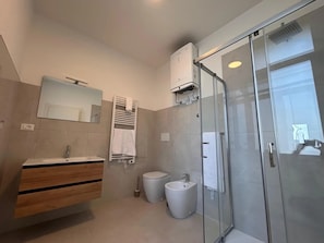 Ein modernes Badezimmer mit Duschkabine aus Glas, einem Waschbecken mit Spiegel und einer Toilette.