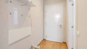 Un passadís amb una porta blanca, una prestatgeria blanca i una planta petita, i una barana blanca.