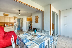 A dining area with a table set for two, a red sofa, and a kitchen in the background. - “L’Escale Marine” – AC, Beach, Sleeps 4 (Sète)