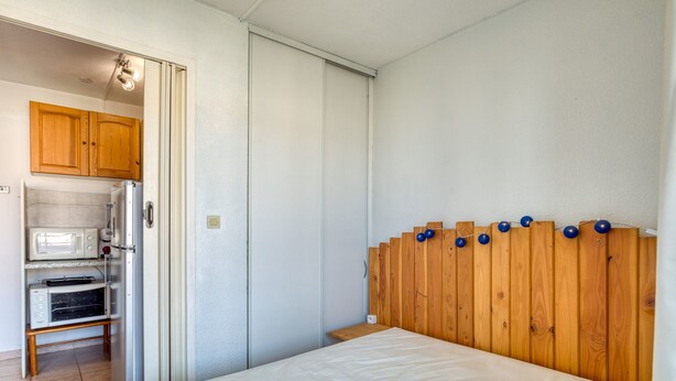 A bedroom with a wooden headboard, a bed, and a kitchenette area with a microwave and toaster. - “L’Escale Marine” – AC, Beach, Sleeps 4 (Sète)