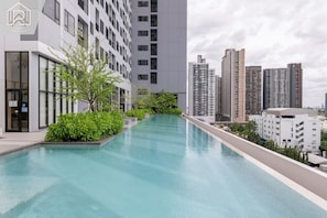 A modern building with a swimming pool, surrounded by greenery and high-rise buildings. - मेट्रो और मॉल के पास आरामदायक आधुनिक कोंडो 10+ दिनों के लिए मासिक प्रवास (Krung Thep Maha Nakhon)