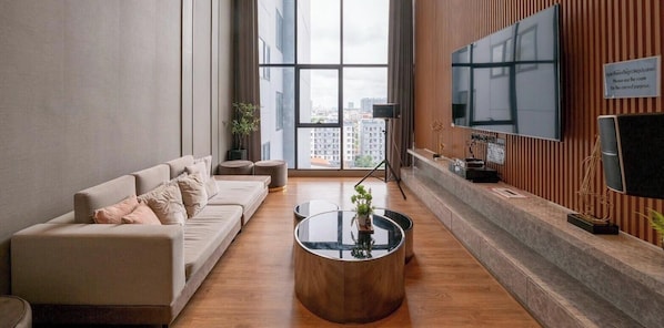 A modern living room with a sofa, a coffee table, a TV, and a view of the city. - मेट्रो और मॉल के पास आरामदायक आधुनिक कोंडो 10+ दिनों के लिए मासिक प्रवास (Krung Thep Maha Nakhon)