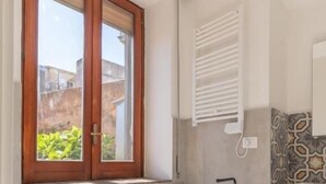 A bathroom with a toilet, bidet, sink, and a window with a view of buildings. - Don Giovanni (Acireale)