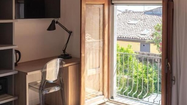 A bedroom with a wooden ceiling, a bed, a desk with a chair, a TV, and a balcony with a view. - Don Giovanni (Acireale)