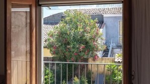 An open sliding door leading to a balcony with a hot tub, a wooden ceiling, and a view of a garden. - Don Giovanni (Acireale)