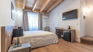 Hotellihuone, jossa on sänky, työpöytä, tuoli, televisio ja pieni jääkaappi.