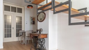 A room with a wooden floor, a desk with a sewing machine, a chair, a table, and a door with frosted glass panels. - Don Giovanni (Acireale)