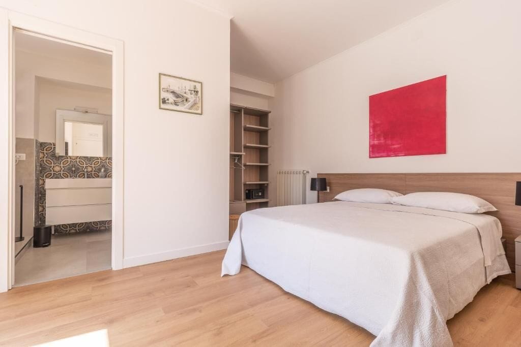 A bedroom with a bed, a red accent wall, a wooden headboard, and a walk-in closet.