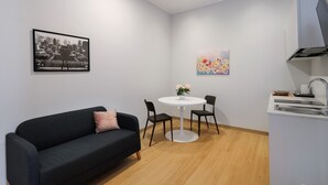 Moderni olohuone, jossa on musta sohva, pyöreä pöytä tuoleineen, keittiöalue, jossa on pesuallas ja kaappeja, sekä kaksi seinälle asennettua taideteosta.