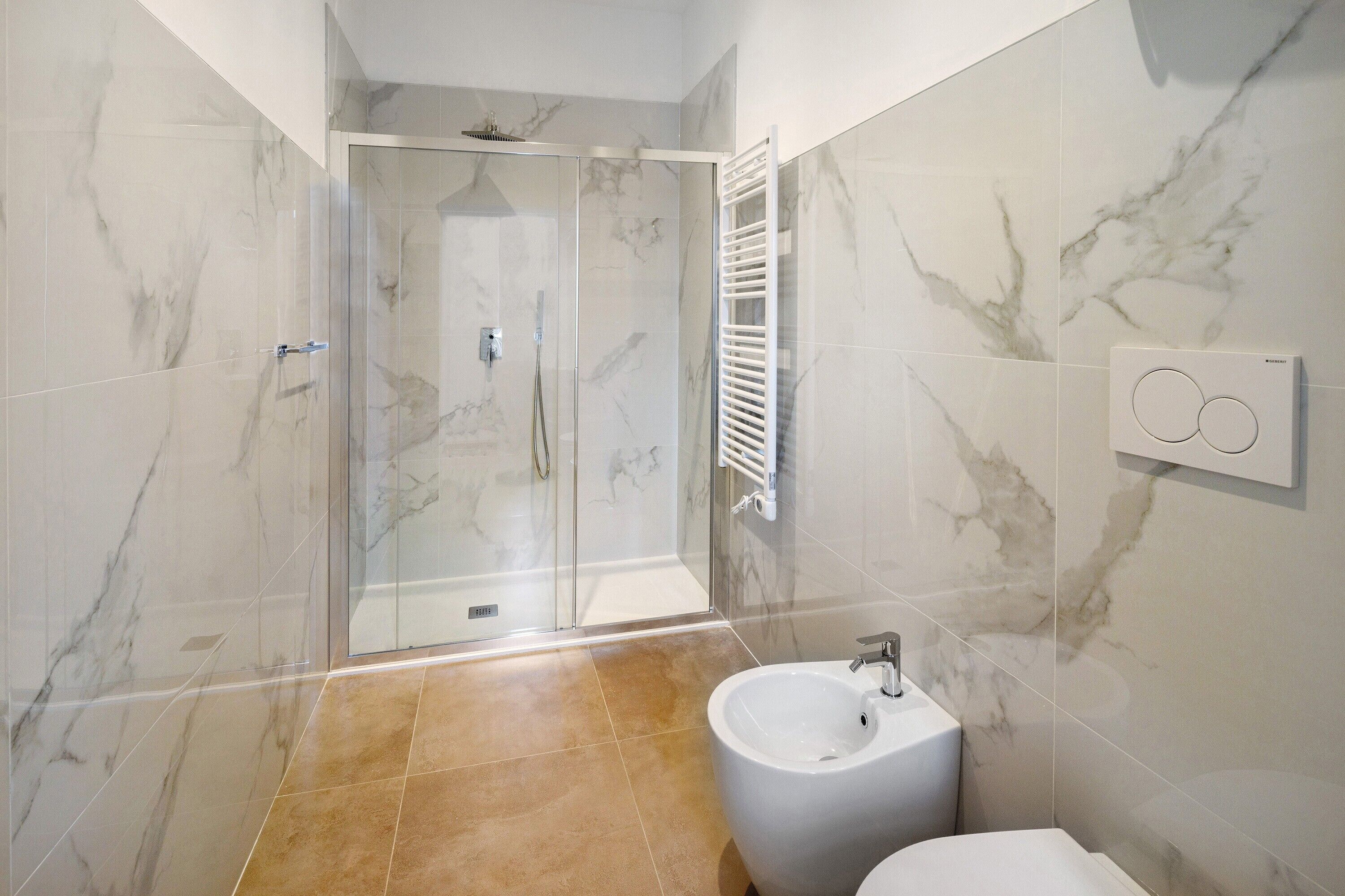 A modern bathroom with a glass-enclosed shower, a white sink, and marble-patterned walls.