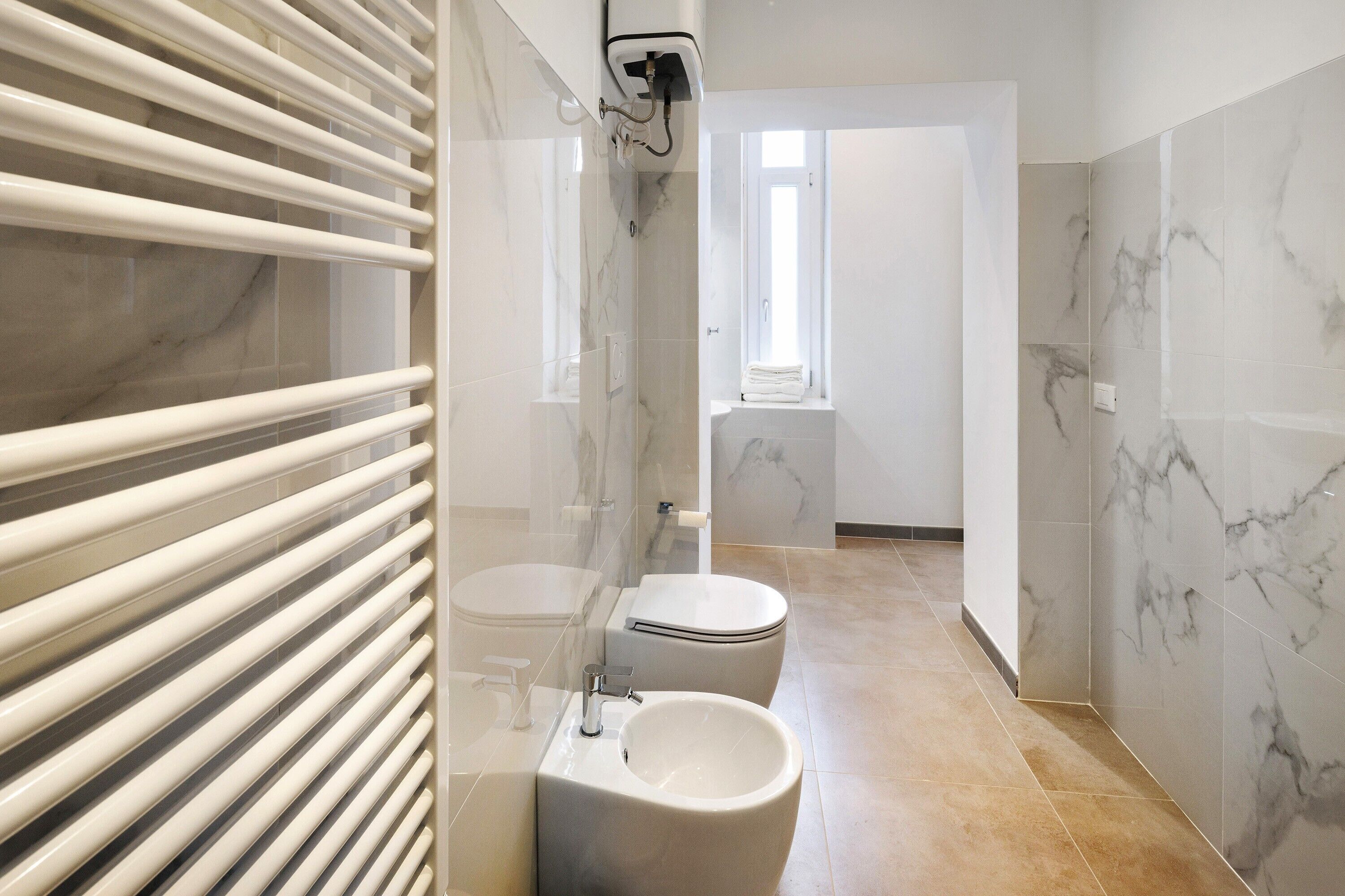 A modern bathroom with a toilet, bidet, and sink, marble walls, and a shower area.