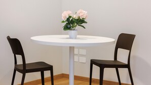 Pyöreä valkoinen pöytä, jossa on ruukussa oleva kasvi, kaksi mustaa tuolia ja seinä, jossa on kukka-aiheinen taulu.