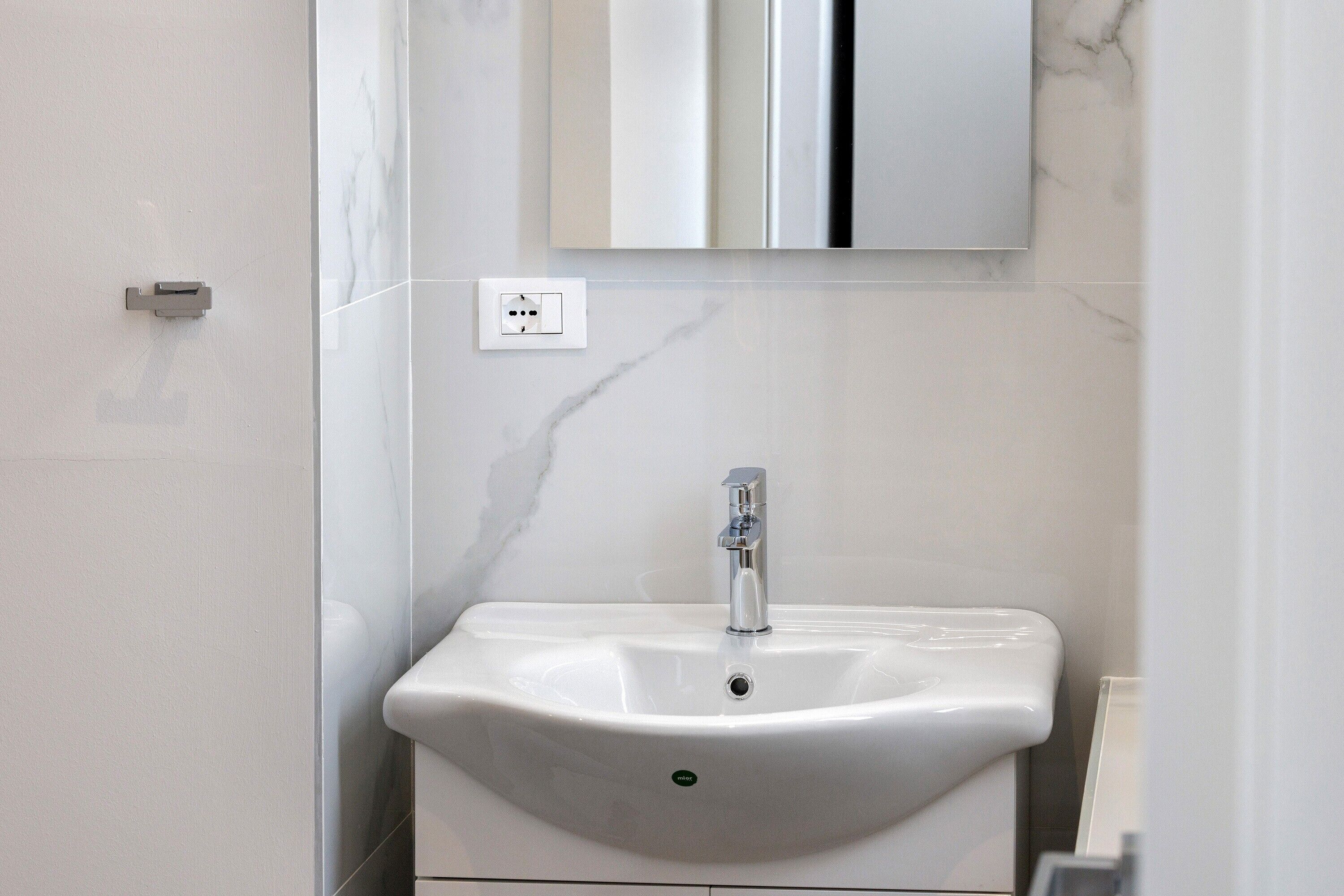 A bathroom with a white sink, a mirror above it, and a marble wall.