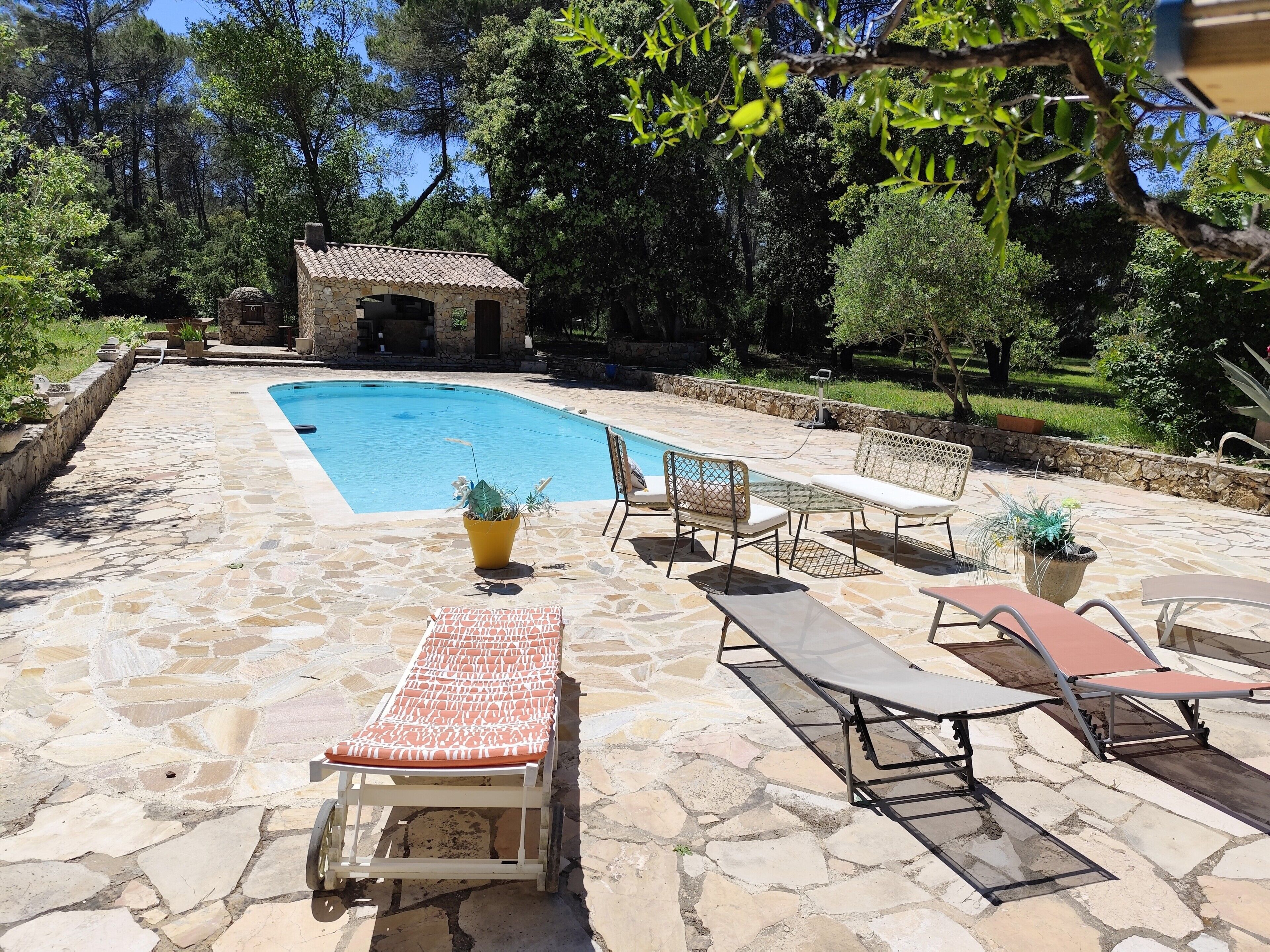 Une piscine en pierre, avec des chaises longues, et un petit bâtiment en pierre en arrière-plan.