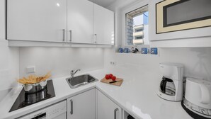 A modern kitchen with white cabinetry, a built-in stove, a sink, and a coffee maker. - 2-Bedroom Vacation Apartment Near the Beach in Westerland (Sylt)