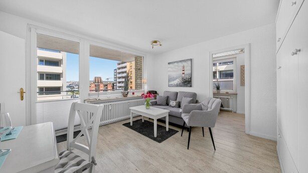 A modern apartment with a living area, dining table, and a view of the city. - 2-Bedroom Vacation Apartment Near the Beach in Westerland (Sylt)