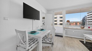 A modern apartment with a dining area, a flat-screen TV, and a balcony with a view of buildings. - 2-Bedroom Vacation Apartment Near the Beach in Westerland (Sylt)