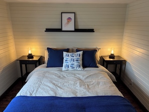 Una camera da letto con un letto, due comodini, una lampada da comodino, un quadro appeso sopra il letto e due lampade a parete.