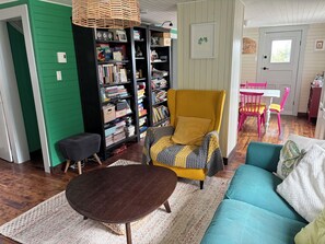 Un salon chaleureux avec une bibliothèque, un fauteuil jaune, un canapé turquoise et une petite table ronde.