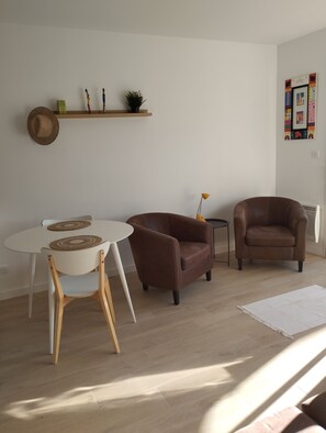 A living room with a round table, two brown leather armchairs, a small side table, a hat on the wall, and a shelf with decorative items. - The Castle (Sommières)