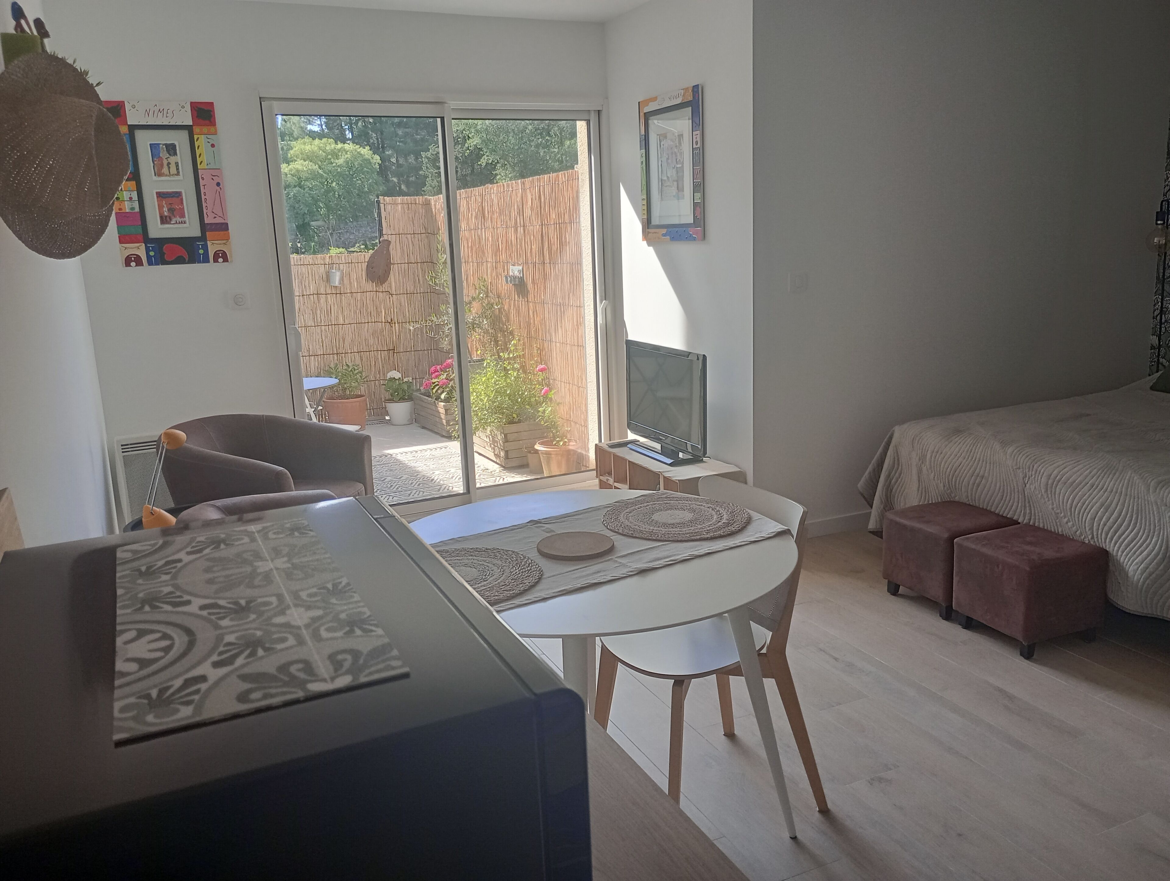 Et værelse med en seng, fjernsyn, et spisebord med stole, en sofa og udsigt til en have gennem en skydedør.