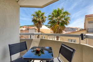 Ein Balkon mit Tisch und Stühlen, Blick auf Palmen und Gebäude im Hintergrund.
