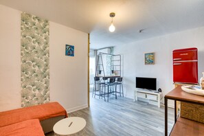 Ein modernes Wohnzimmer mit einer Couch, einem Fernseher, einem roten Kühlschrank und einer Leiter im Hintergrund.