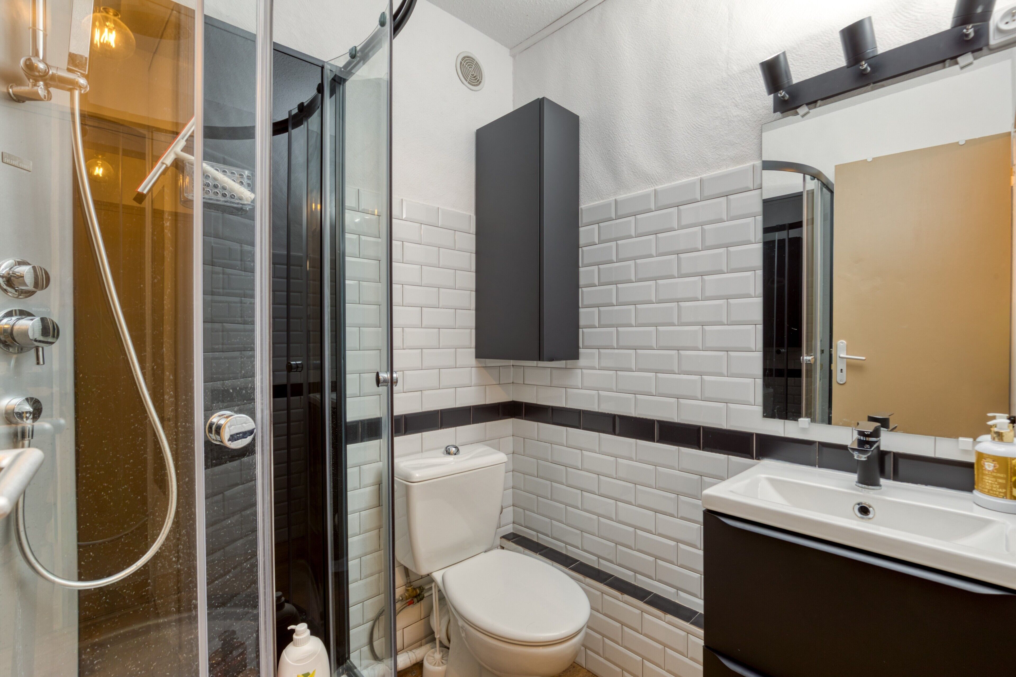 A modern bathroom with a glass shower enclosure, a white toilet, a black cabinet, and a sink with a mirror above it.