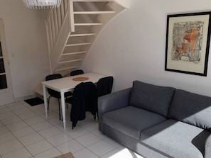 Ein zeitgemäßer Wohnraum mit grauem Sofa, einem weißen Esstisch mit Stühlen und einer Treppe.