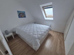 Ein Schlafzimmer mit einem Bett, einem Nachttisch, einem kleinen Tisch, einem Fenster und einem Bild an der Wand.