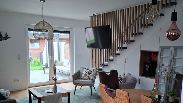 Ein stilvolles Wohnzimmer mit einer Couch, Sesseln, einem Couchtisch, einem Fernseher und einer Treppe mit Holzwand.