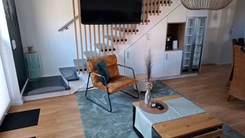 Een moderne woonkamer met een flatscreen televisie, een bruine leren fauteuil, een houten salontafel en een trap met houten leuningen.