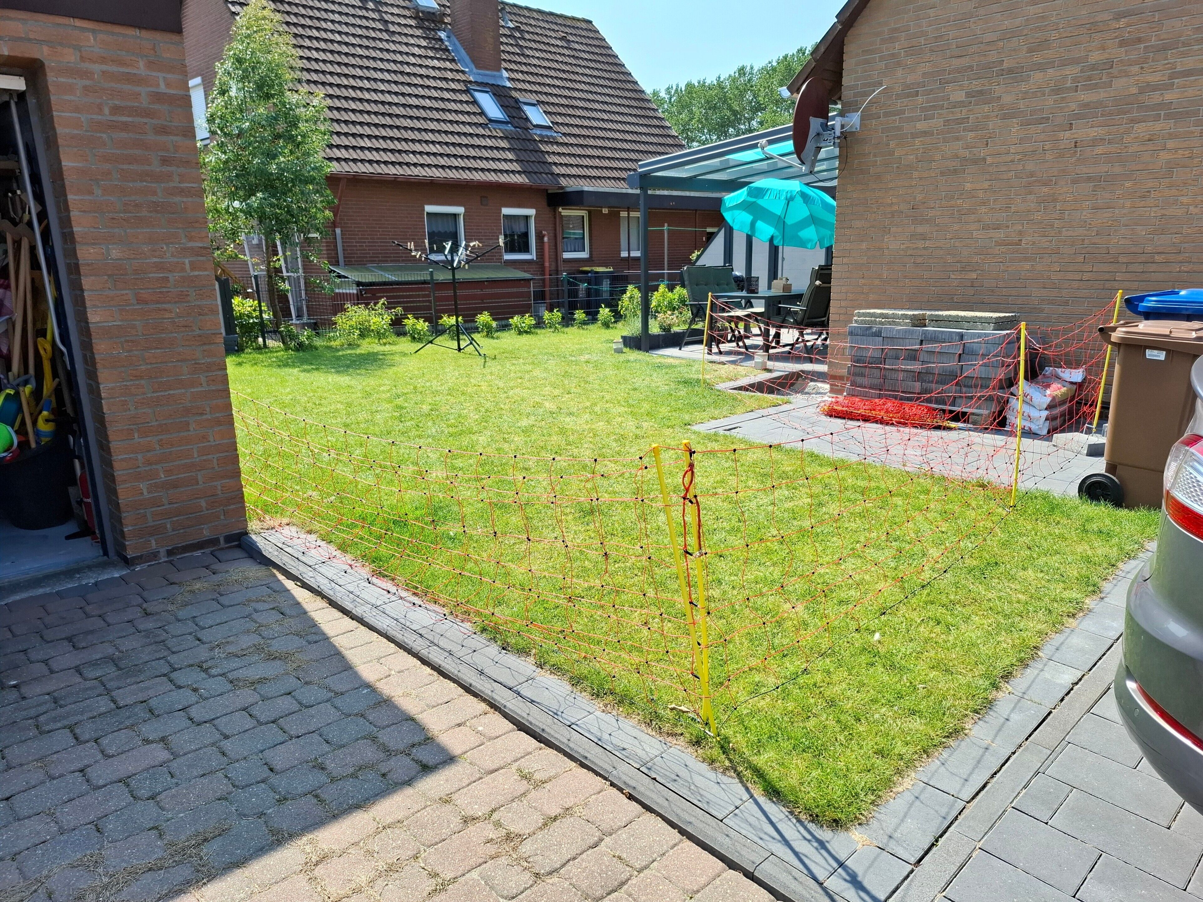 Ein Wohnhausgarten mit Rasen, einem eingezäunten Spielbereich und einem in der Nähe stehenden Auto.