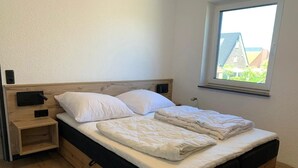 Ein Einzelbett mit Holz Kopfteil, ein Nachttisch und ein Fenster mit Blick auf Grünflächen.