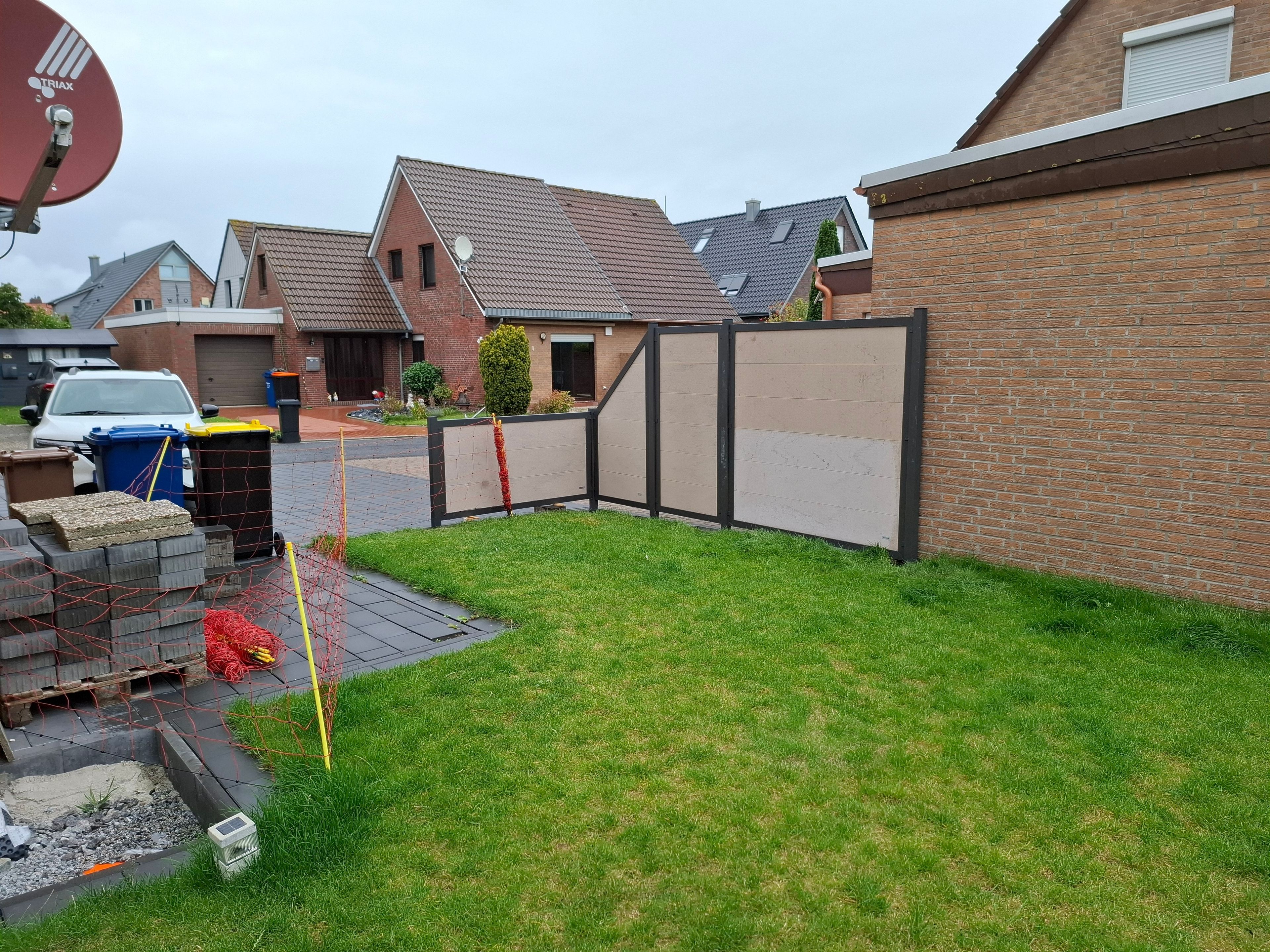 Un quartier résidentiel avec une maison en briques, une cour clôturée et une antenne parabolique.