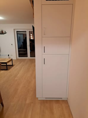 Une pièce avec une armoire blanche, une table en bois et une porte-fenêtre coulissante donnant sur une autre pièce.