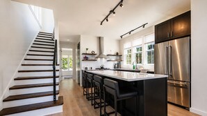 Una cocina moderna con una isla central, electrodomésticos de acero inoxidable y una escalera que sube a otro nivel.