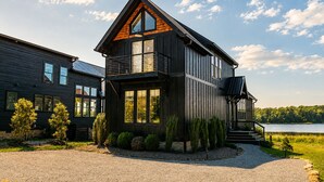 Una casa moderna de dos pisos con balcón, ventanas amplias y vista a un lago.